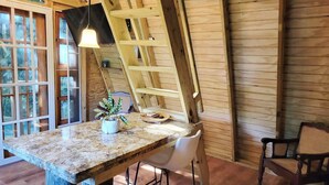 Un interior de madera con mostrador de cocina, sillas blancas y una escalera.