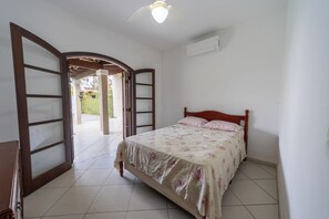 Ein Schlafzimmer mit einem Bett, einem Holz-Kopfteil, einem Deckenventilator und einer offenen Tür zu einem Balkon.