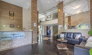 Un hall d’entrée moderne comprenant un comptoir d’accueil, un escalier, un espace détente avec un canapé et une rambarde en verre.
