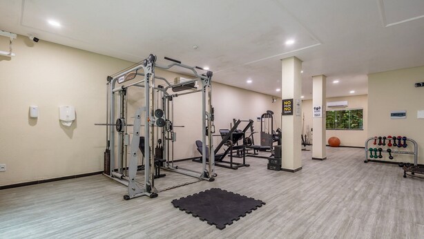 A gym with exercise equipment, a black mat, and a wall-mounted dumbbell rack. - Apts in Condo w/ Pool and Gym 450m From the Beach - SBH (Bombinhas)