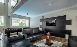 A modern living room with a black leather sofa, a wooden coffee table, and a flat-screen TV mounted on a black wall. - Apts in Condo w/ Pool and Gym 450m From the Beach - SBH (Bombinhas)