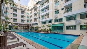 A multi-story hotel with a swimming pool, lounge chairs, and a bar. - Apts in Condo w/ Pool and Gym 450m From the Beach - SBH (Bombinhas)