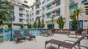 A poolside area with lounge chairs, a pool, and a building with balconies. - Apts in Condo w/ Pool and Gym 450m From the Beach - SBH (Bombinhas)