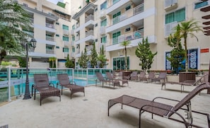 Un espace aménagé au bord de la piscine, avec des chaises longues, une piscine et un bâtiment doté de balcons.