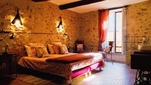 Een slaapkamer met een groot bed, twee bedlampen, een houten vloer, een raam met gordijnen en een naaimachine.