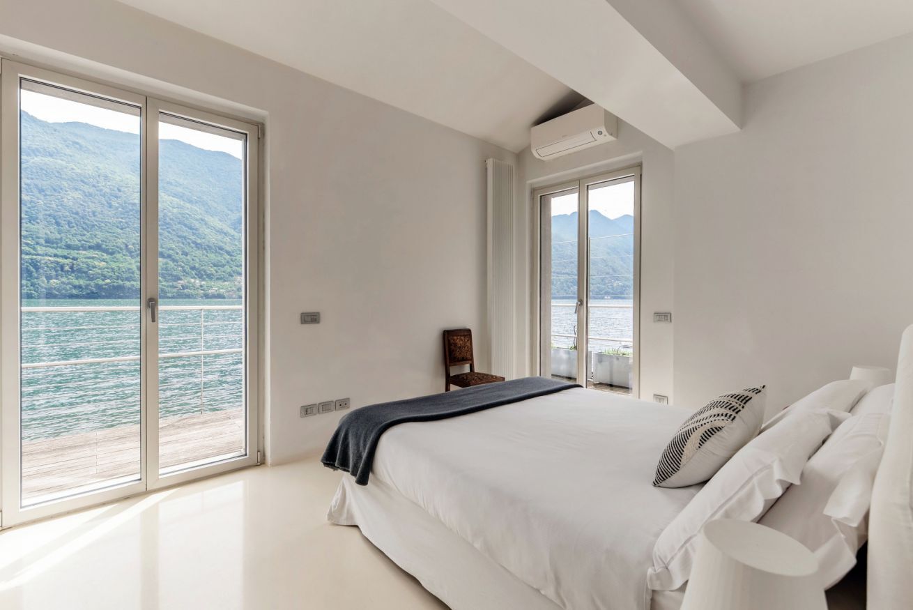 Ein Schlafzimmer mit Bett, einem Sessel und Blick auf einen See und Berge.