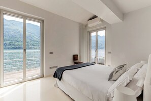 A bedroom with a bed, a chair, and a view of a lake and mountains. - Villa Irene - Breathtaking view of Lake Como (Brienno)