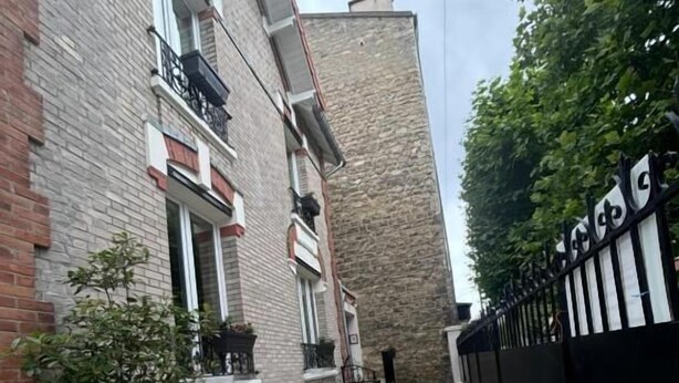A narrow outdoor corridor with a tiled floor, a potted plant, and a chair. - Pavillon 92 (La Garenne-Colombes)