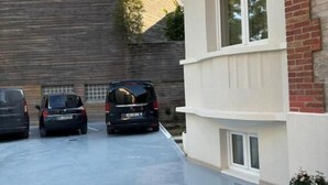 A parking area with three cars, a building with a brick facade, and a white structure with windows. - Pavillon 92 (La Garenne-Colombes)