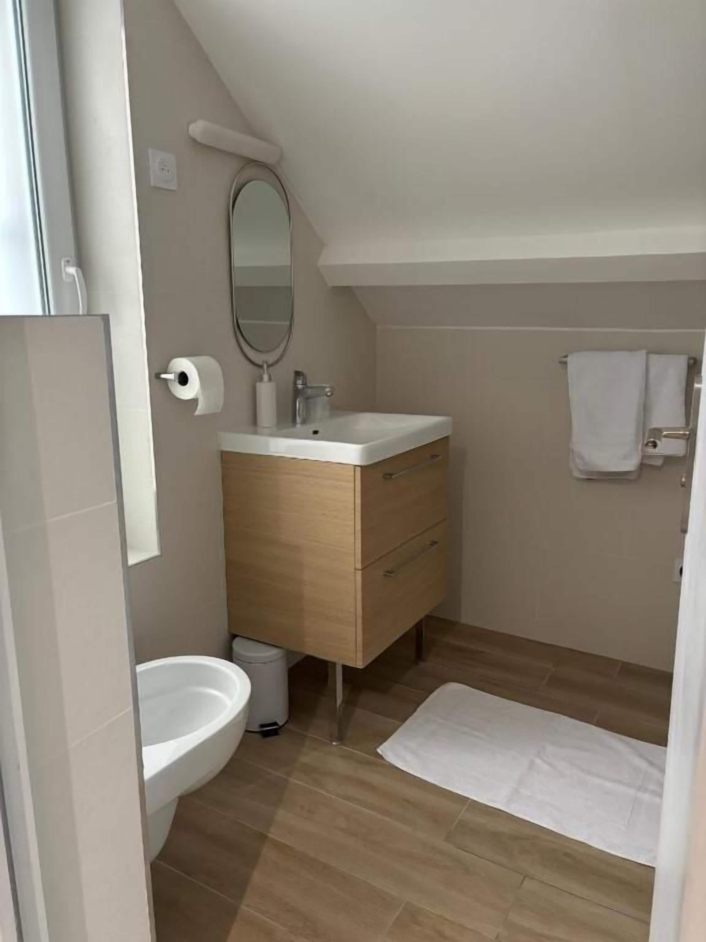 A modern bathroom with a wooden vanity, a white sink, and a mirror.