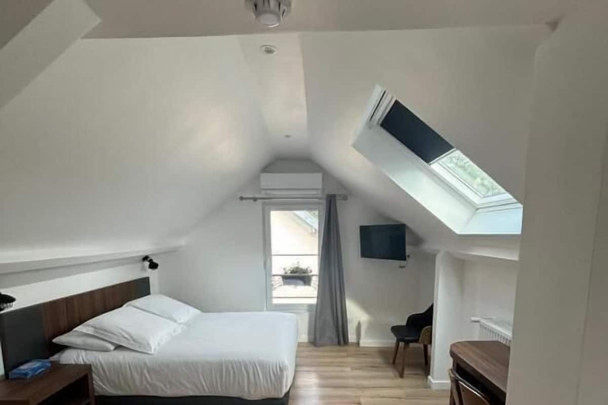 A bedroom with a sloped ceiling, a bed, a desk, and a TV.