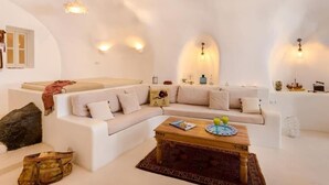 A modern living room with a white sofa set, a wooden coffee table, and decorative wall sconces. - Cave at White Rock  Private  jacuzzi  (Santorini)