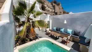 A pool area with a seating arrangement and a palm tree. - Cave at White Rock  Private  jacuzzi  (Santorini)
