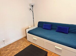 A small, single-bed room with a blue mattress, two pillows, a bedside table, and a floor lamp. - Studio with veranda, 5min walk to the beach (Nice)