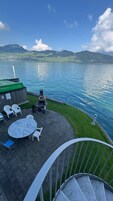 Una terraza con mobiliario exterior, una parrilla y vistas a un lago con montañas al fondo.