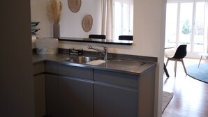 A modern kitchen with a stainless steel sink, a built-in oven, and a dining area with a black chair and a table. - Line UP - 2,5 Zi Whg mit Seeanstoss - Beckenried (Beckenried)