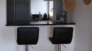 A modern kitchen with a black countertop, two black bar stools, and a woven light fixture. - Line UP - 2,5 Zi Whg mit Seeanstoss - Beckenried (Beckenried)