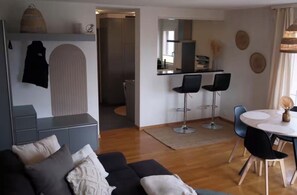A modern living room with a sofa, a dining area with a table and chairs, and a kitchen in the background.
