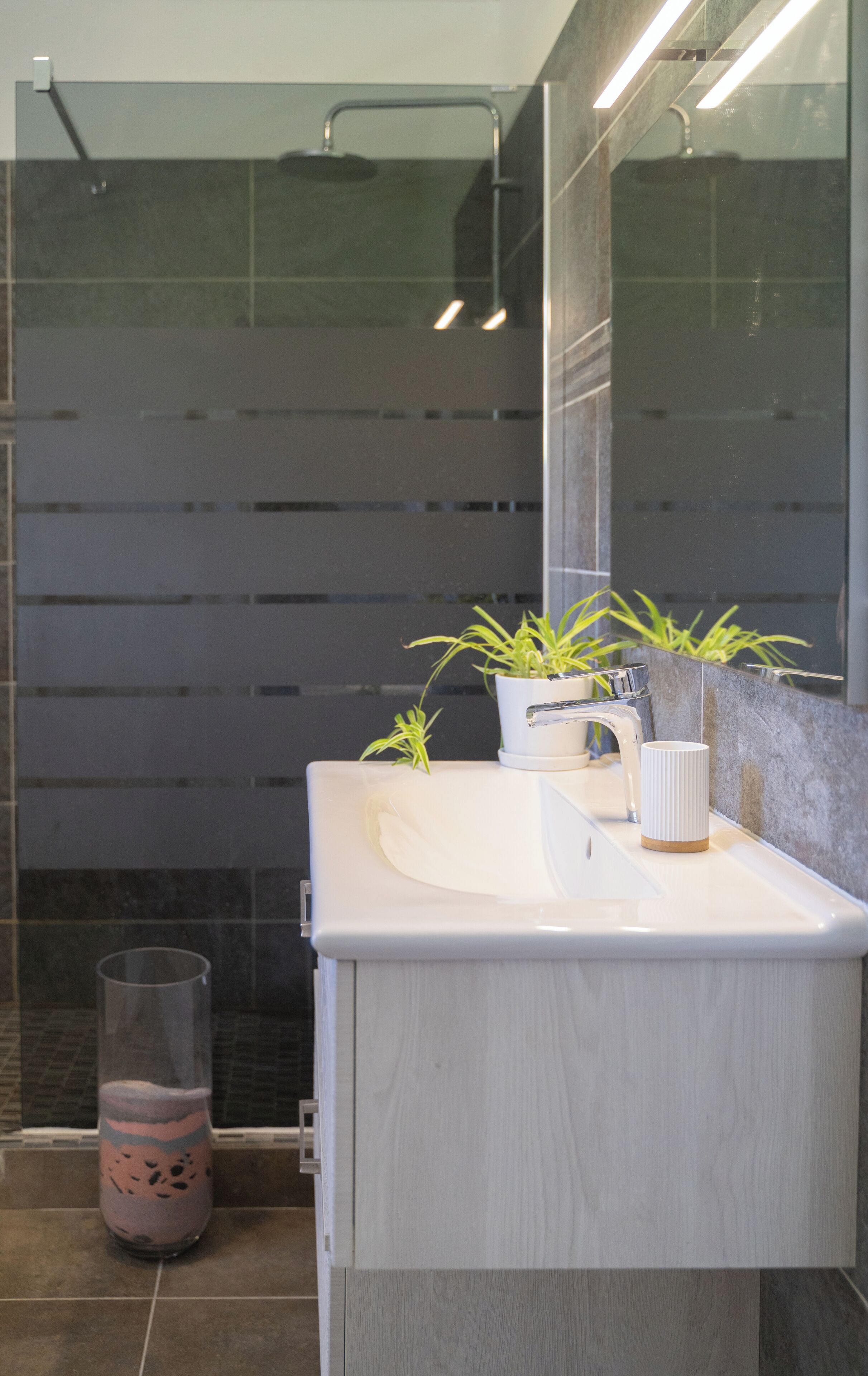 A modern bathroom with a white sink, a mirror, and a shower area.