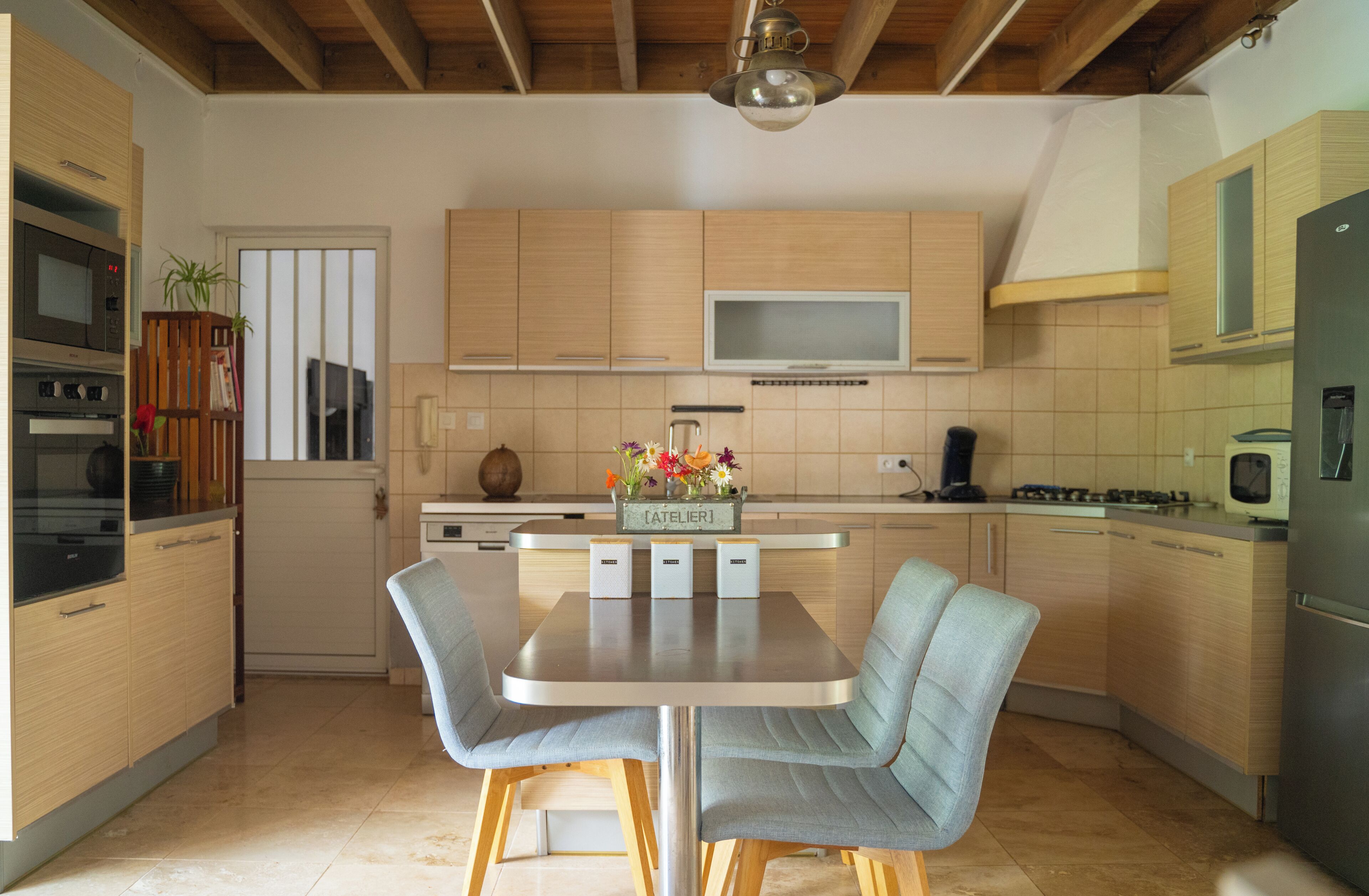 Een moderne keuken met houten kastjes, een centraal eiland met stoelen, een inbouwoven en een magnetron.