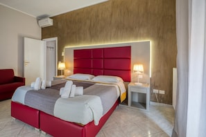 Ein Hotelzimmer mit einem roten Bett, zwei Nachttischen mit Lampen, einer roten Couch und einer Holzwand.