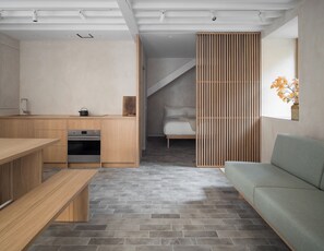 A modern kitchen with wooden cabinets and a built-in oven, a dining area with a bench, and a living space with a sofa and a decorative vase. - Porteous Studio - An apartment for two in the heart of Edinburgh's Old Town. (Edinburgh)