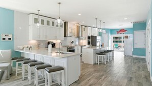 Una cocina amplia con armarios blancos, una isla central con taburetes y iluminación colgante.