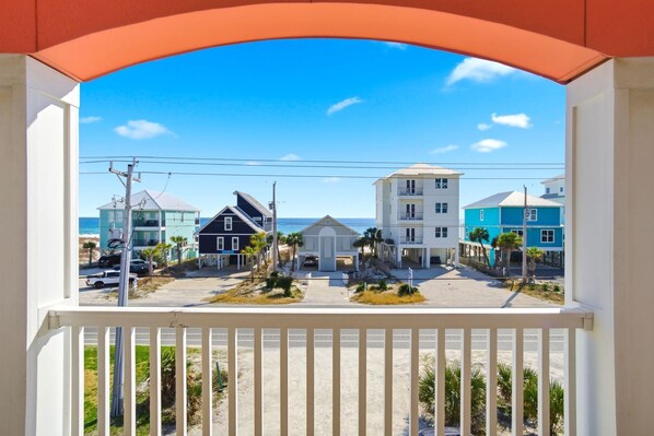 A balcony with a view of a beachfront area, including buildings and a clear sky. - Graceful Memory (Gulf Shores)