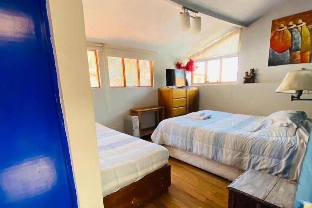 Quarto com duas camas, piso de madeira, cômoda, escrivaninha e um quadro na parede.
