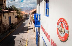 Rua estreita com um edifício de hostel à direita, exibindo uma placa com a inscrição 'Flying Dog Hostels'.