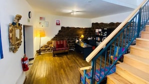 A cozy living room with a fireplace, wooden flooring, a staircase with blue railings, and a bookshelf. - Flying Dog Hostel Cusco (Cusco)
