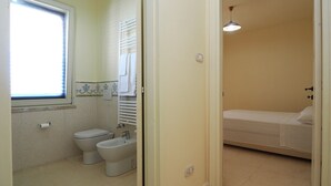 Une salle de bain avec des toilettes, un bidet et un lavabo, et une chambre avec un lit.