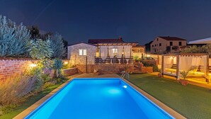 Une piscine bordée d’un côté par un mur de briques et de l’autre par une pelouse agrémentée d’une pergola.
