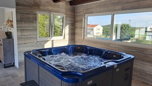 Un bain à remous dans une pièce dotée de grandes fenêtres, de murs en pierre et d’un plafond en bois.