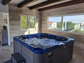 A hot tub in a room with large windows, stone walls, and a wooden ceiling. - Villa Nicoletta (Polaca)