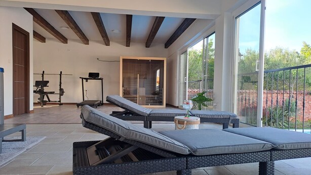Un salon moderne doté d’une grande porte-fenêtre coulissante donnant sur un balcon, d’un espace dédié à l’exercice physique avec du matériel d’entraînement, et d’un coin salon confortable avec des fauteuils.