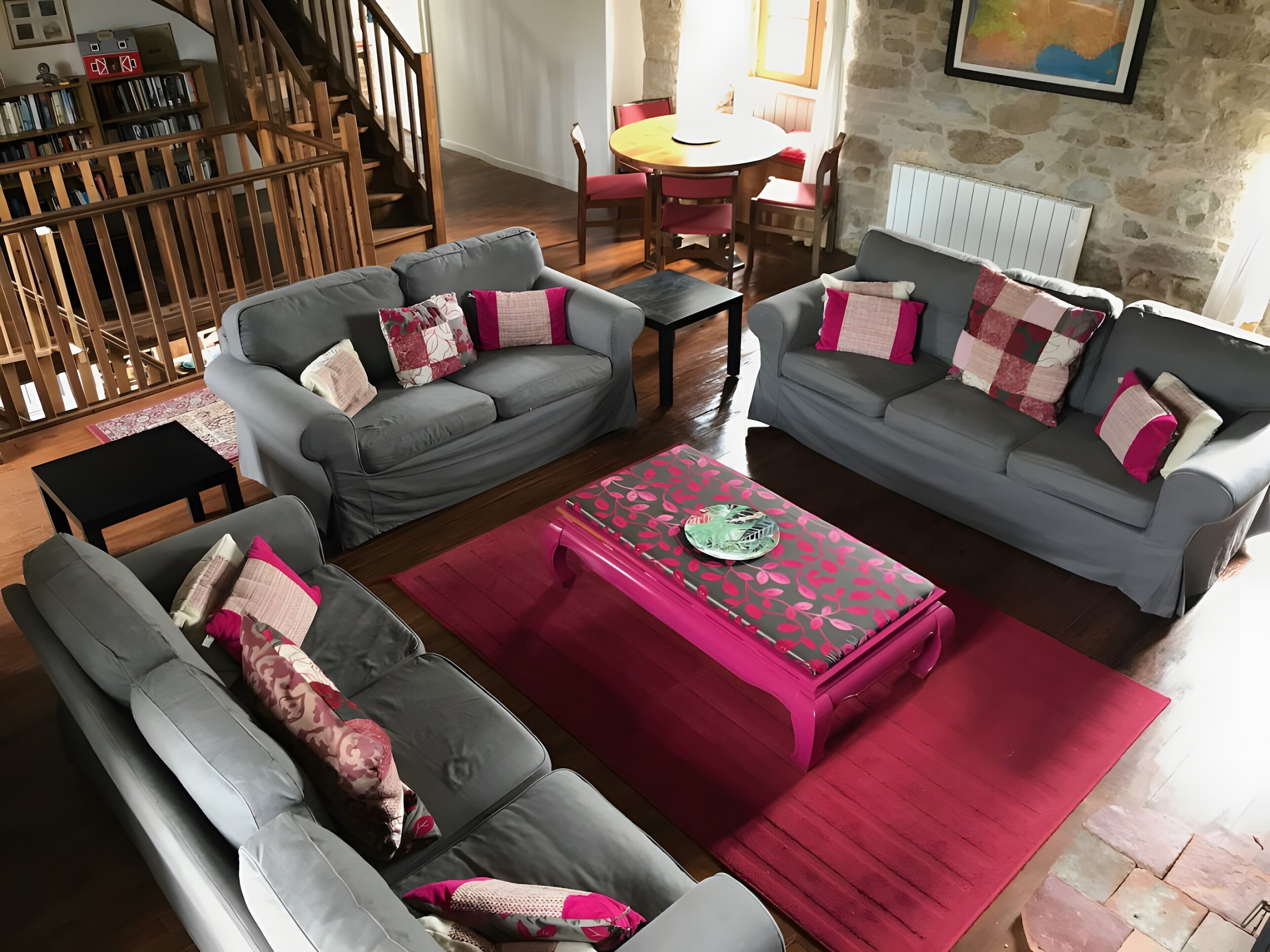 A living room with two grey sofas, a red coffee table, and a staircase leading to a dining area.