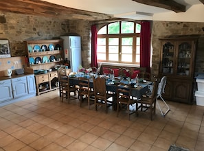 Un comedor rústico con pared de piedra, muebles de madera y un gran ventanal con cortinas rojas.