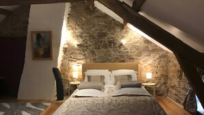 Une chambre avec un mur en pierre, un lit avec une literie à motifs, deux tables de chevet avec des lampes et un plancher en bois.