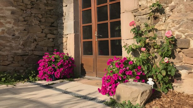 Un bâtiment en pierre avec une grande porte en bois, des fleurs roses et une lanterne blanche.