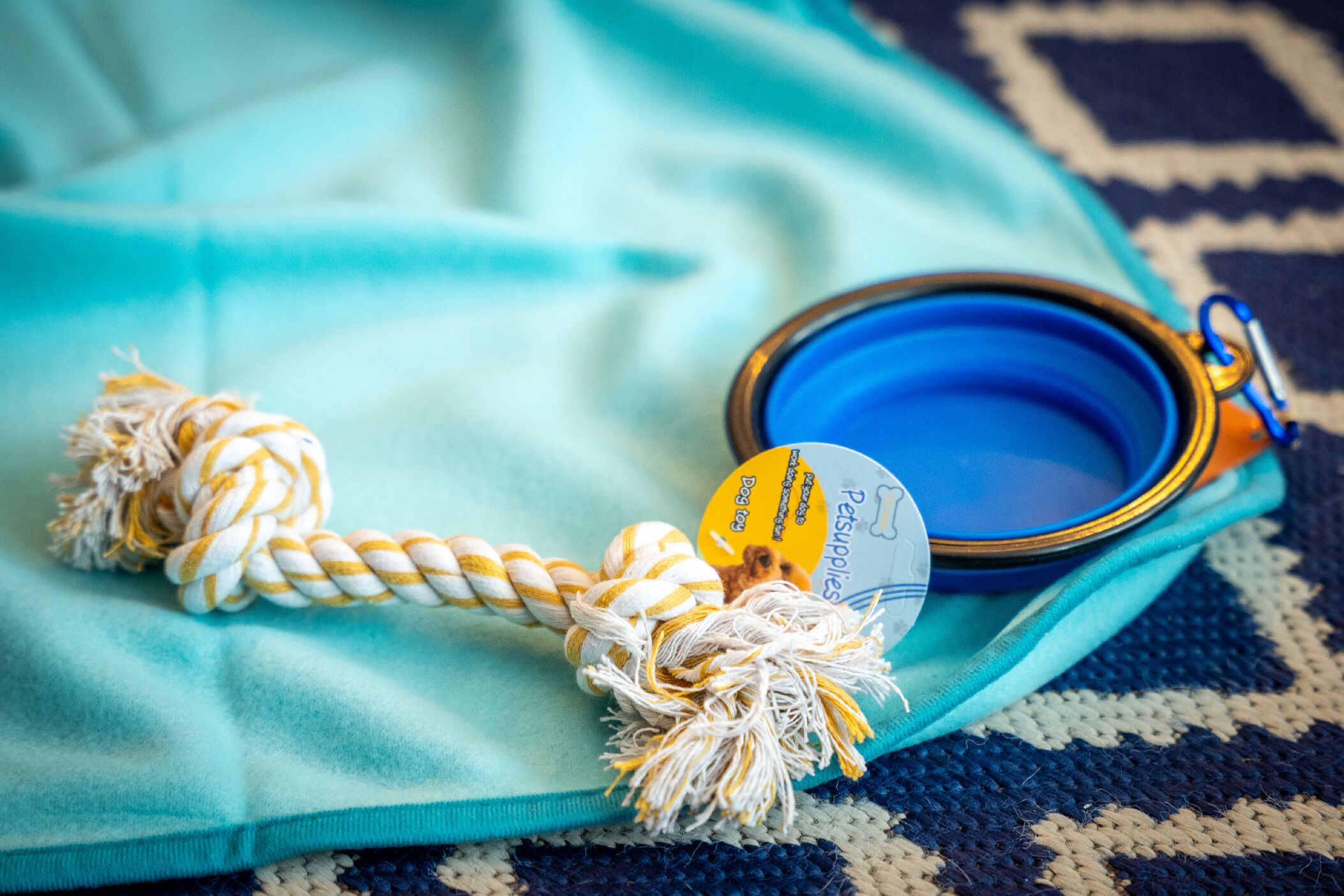 A pet supplies bag with a blue lid and a tag, placed on a teal fabric.