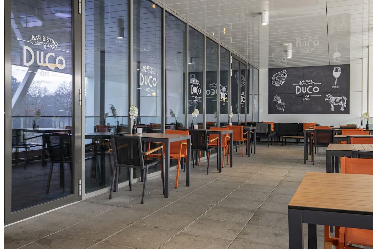 A modern restaurant interior with glass partitions, orange chairs, and black tables.