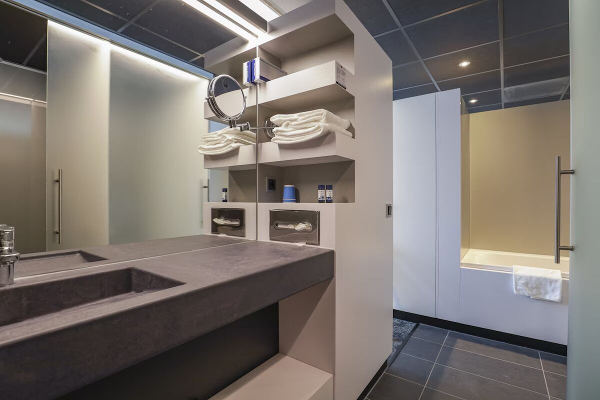 A modern bathroom with a large sink, a mirror, and shelves with towels.