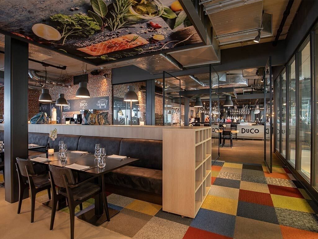 A modern restaurant interior with a bar area, seating arrangements, and a colorful floor pattern.