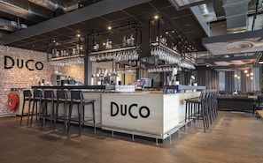 A bar area with a wooden counter, bar stools, and shelves of glasses and bottles. - Relax in Style at our Modern Room Close to Autotron and Speeltuin Elckerlyc (Oss)
