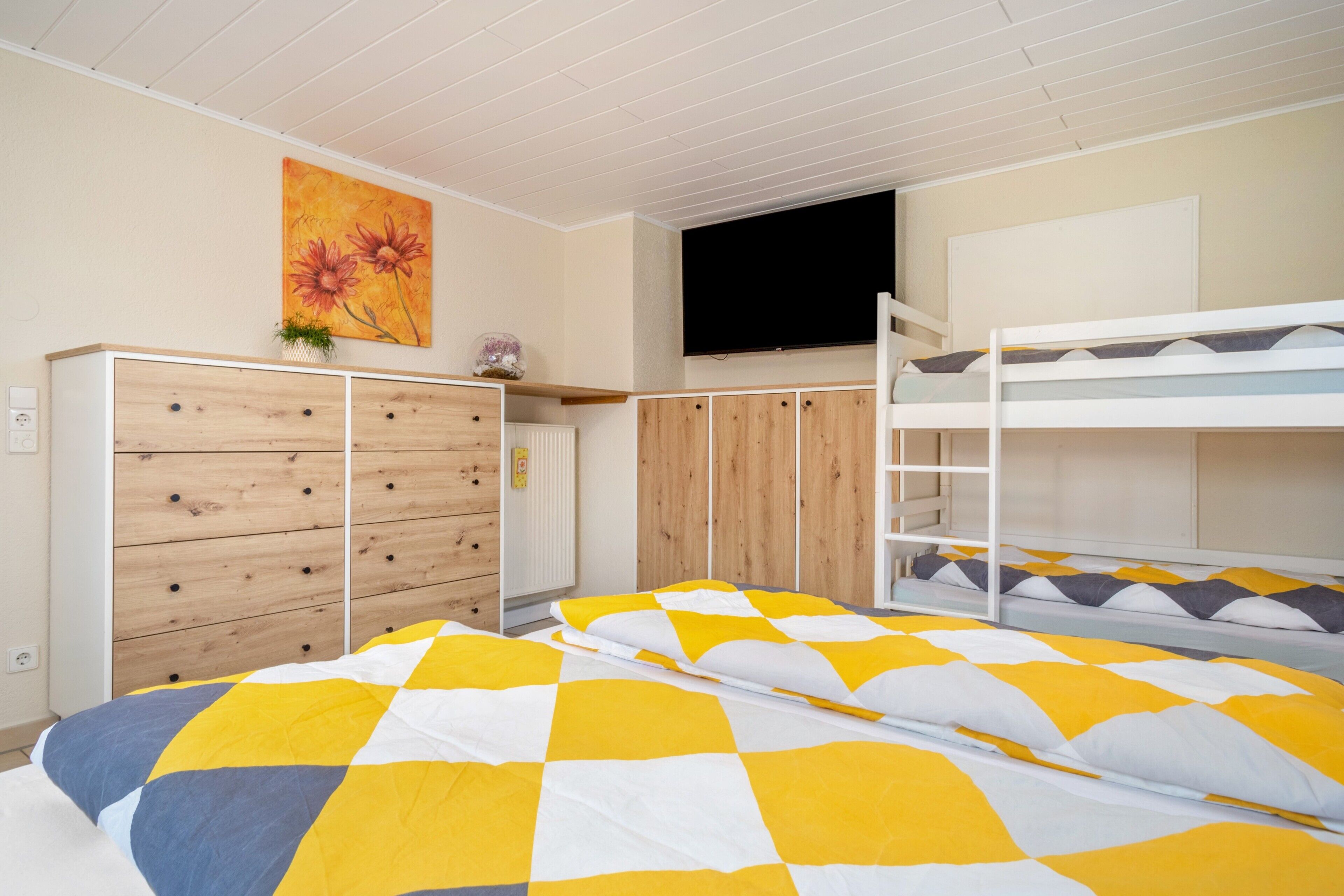 A bedroom with bunk beds, a wooden wardrobe, a flat-screen TV, and a painting on the wall.