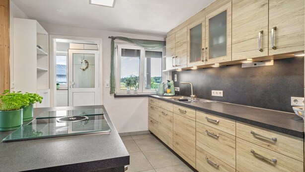 Una cocina con armarios de madera, encimera negra, estufa integrada y ventana con vistas.