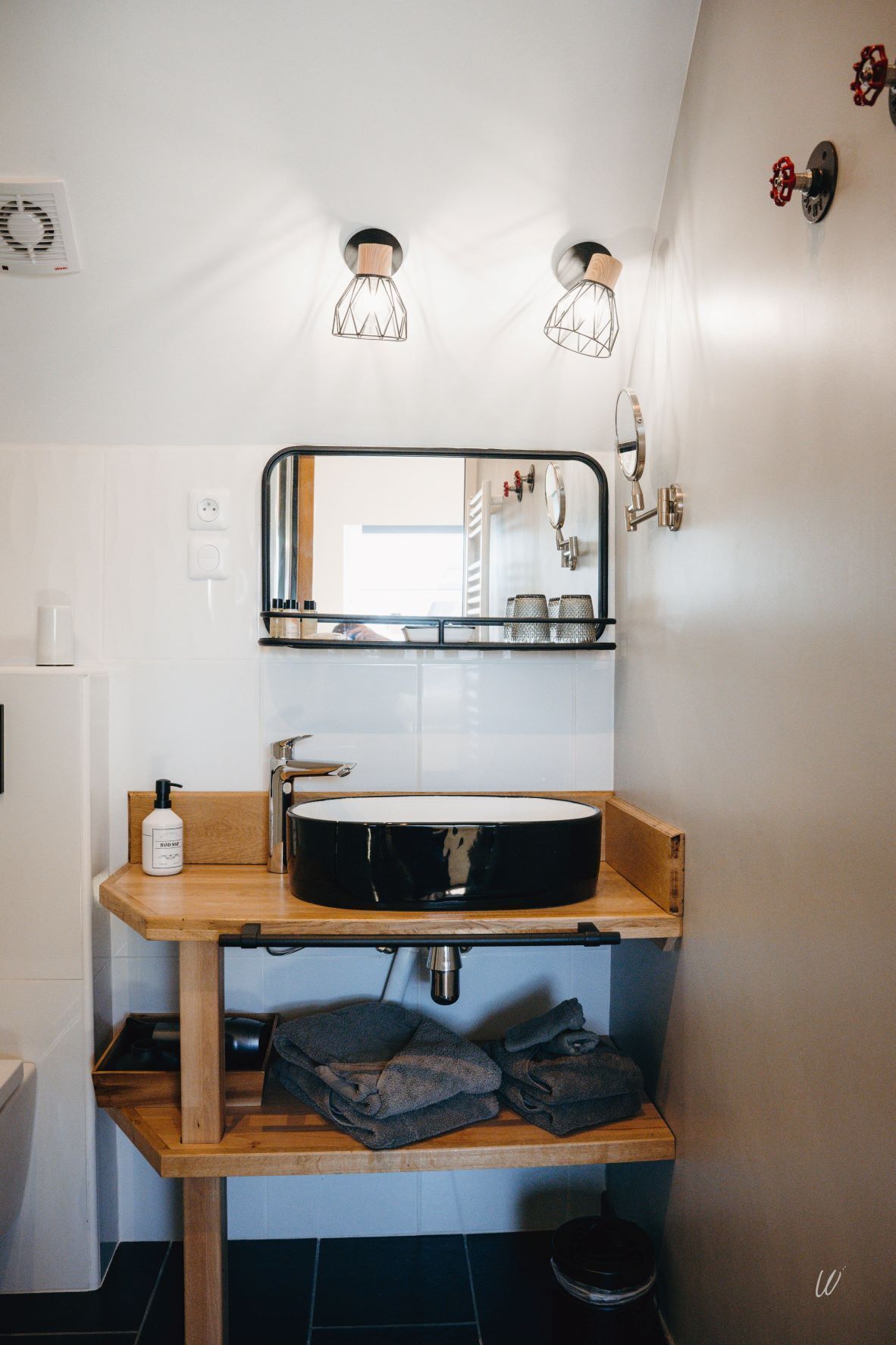 A modern bathroom with a round black sink, wooden vanity, and two wall-mounted light fixtures.