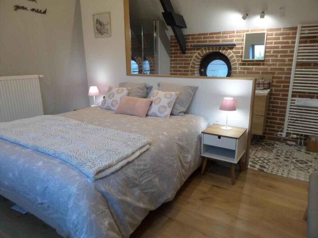 A bedroom with a bed, bedside tables, a mirror, and a brick wall.