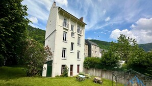 Ein zweistöckiges Gebäude mit grüner Tür und Fenstern, umgeben von einem gepflegten Rasen und Bäumen.